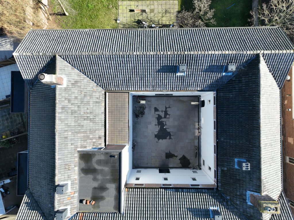 Luchtfoto van een wooncomplex met pannendaken en platte dakdelen rondom een binnenplaats