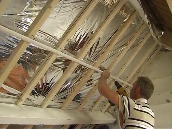 Medewerker bevestigt houten latten aan de binnenzijde van een schuin dak met reflecterende folie