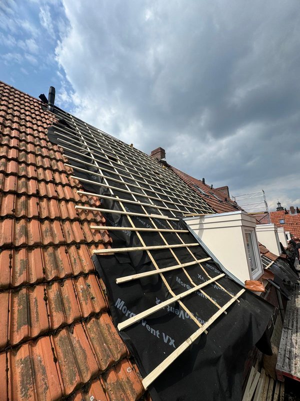 Vrijgelegd pannendak met zichtbaar latwerk en dakfolie naast een dakkapel