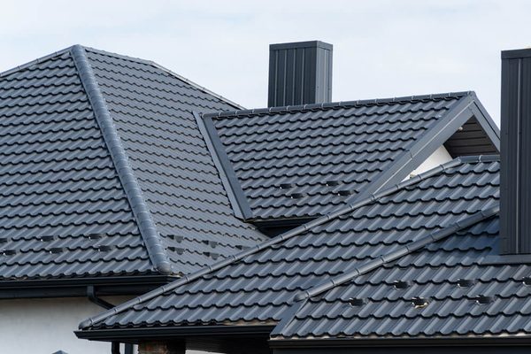 Donkere dakpannen op meerdere dakvlakken met nokpannen en schoorstenen